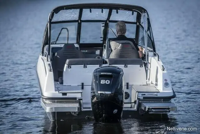 A man sits at the helm of a white boat with a Mercury 80 outboard motor, navigating calm waters.